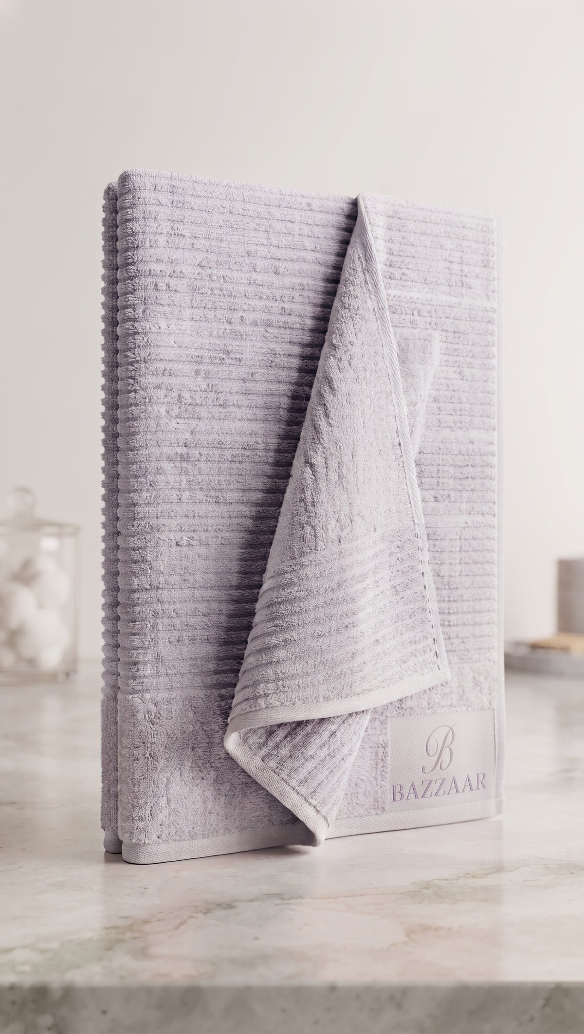 Light grey textured towel with horizontal raised lines, folded upright with Bazzaar branding visible